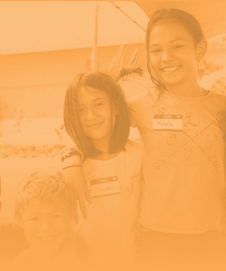 Three young kids of varying heights stand with arms around each other.