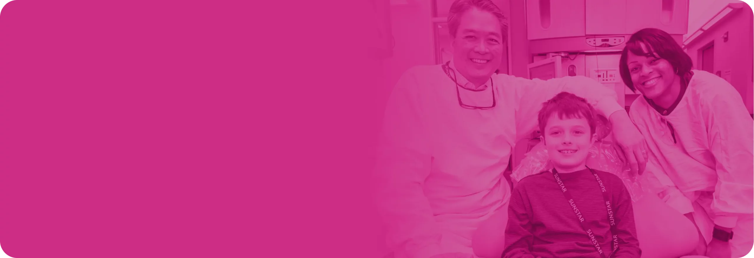 A young boy smile in an exam chair with a male and female provider on either side.